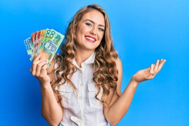 Avustralya doları tutan genç sarışın kız başarıyı mutlu bir gülümsemeyle ve kazanan yüz ifadesiyle kutluyor. 