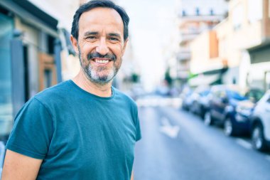 Orta yaşlı, sakallı, açık havada mutlu gülümseyen bir adam.