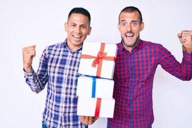 Genç eşcinsel iki adam ellerinde hediyeler tutarak gururla haykırıyorlar zaferi kutluyorlar ve kollarını kaldırarak çok heyecanlılar. 