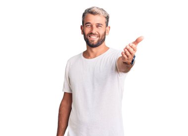 Genç, sarışın, sıradan tişörtler giyen, dostça gülümseyen, selamlaşmak ve selamlamak için tokalaşan bir adam. başarılı iş. 