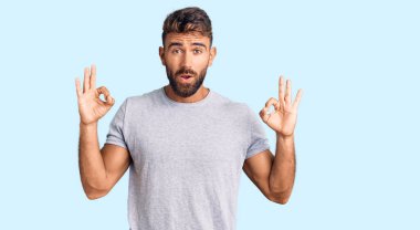 Gündelik kıyafetler giyen genç İspanyol adam şaşırmış ve şok olmuş görünüyor. Tamam sembolünü parmaklarıyla yapıyor. çılgın ifade 