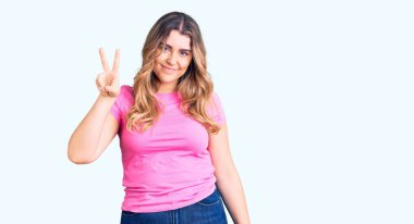 Genç beyaz kadın spor giysisi giyiyor. İki numarayı gösterip işaret ederken kendine güvenen ve mutlu bir şekilde gülümsüyor.. 