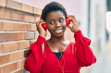 Genç Afrikalı Amerikalı kadın gülümseyerek şehirde kulaklık takarak müzik dinlemekten mutlu oluyor..