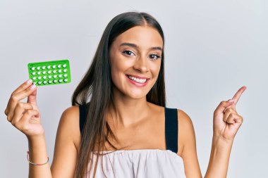 Elinde doğum kontrol hapları tutan genç İspanyol kadın gülümsüyor. 