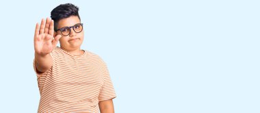 Günlük kıyafetler ve gözlük takan küçük çocuk avuç içiyle şarkı söylemeyi kesiyor. Yüzünde olumsuz ve ciddi bir jest olan uyarı ifadesi. 