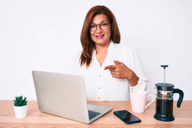 Orta yaşlı esmer, ispanyol iş kadını ofiste çalışıyor, gülümsüyor. 