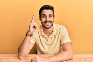 Gündelik giysiler giymiş genç İspanyol adam masaya oturmuş başarılı bir fikirle işaret ediyor. Heyecanlı ve mutlu. Bir numara.. 