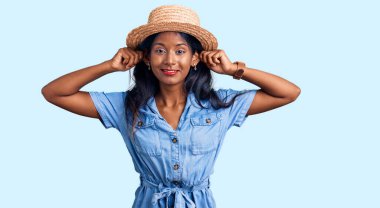 Yaz şapkası takan genç Hintli kız parmaklarıyla kulaklarını çekiyor, komik bir jest. deneme sorunu 