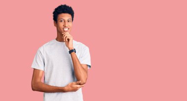 Gündelik giysiler giymiş genç Afro-Amerikan adam kameraya kendinden emin bakıyor kollarını kavuşturmuş ve çenesini kaldırmış bir şekilde gülümsüyor. Olumlu düşünmek. 