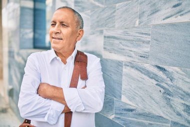 Kıdemli işadamı gülümsüyor. Şehrin duvarına yaslanıyor..