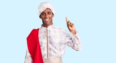 Gelenek giyinmiş Afrikalı yakışıklı bir adam Sherwani sari elbisesi giyiyor ve bir numaralı parmağını gösterip gülümserken kendinden emin ve mutlu.. 