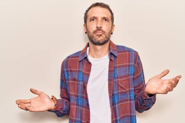 Sıradan kıyafetler giyen, elleri ve kolları havada, kafası karışmış genç ve yakışıklı bir adam. şüphe kavramı. 