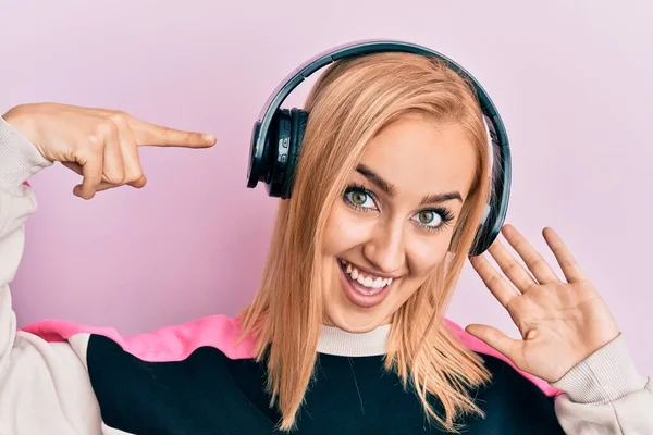 美しい白人女性は 手と指で幸せなポインティングを笑顔ヘッドフォンを使用して音楽を聴く — ストック写真