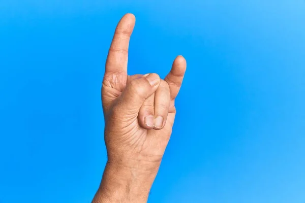 Ręka Starszego Hiszpana Nad Niebieskim Odizolowanym Tłem Gestykulująca Symbolem Rock — Zdjęcie stockowe