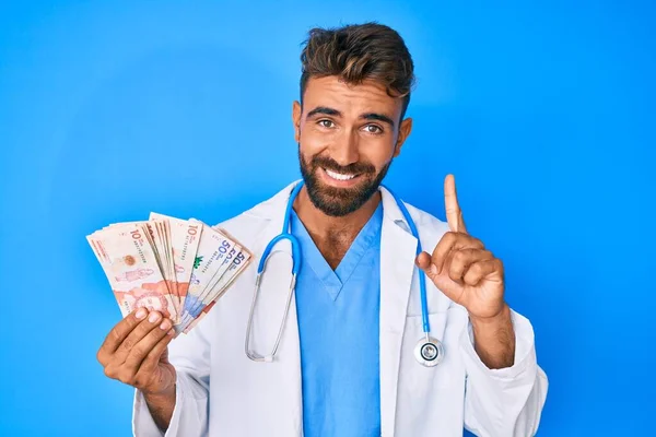 Joven Hispano Vistiendo Uniforme Médico Sosteniendo Pesos Colombianos Sonriendo Con —  Fotos de Stock