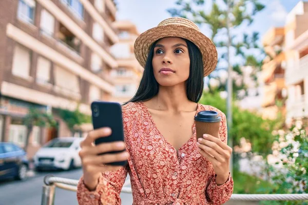 African american tourist woman with serious expression using smartphone and drinking coffee at the city.