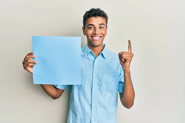 若いですハンサムなアフリカ系アメリカ人男性保持青い空のバナー笑顔でアイデアや質問を指差す指で幸せな顔 ナンバーワン — ストック写真