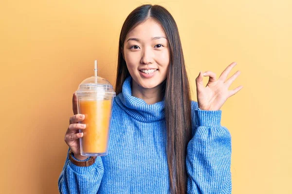 年轻美丽的中国女人喝着一杯橙汁 手拿着手签 微笑着表示友好的姿态 是极好的象征 — 图库照片