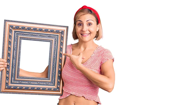 Young Blonde Woman Holding Empty Frame Smiling Happy Pointing Hand — Stock Photo, Image