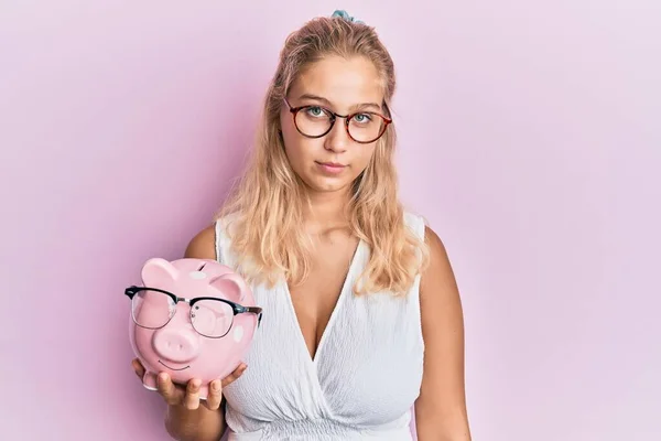 Jong Blond Meisje Holding Piggy Bank Met Bril Denken Houding — Stockfoto