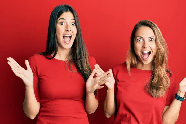 西班牙裔家庭的母亲和女儿身穿红色背景的休闲装 兴奋地举起双臂 睁开眼睛尖叫 庆祝自己的成功 获奖者概念 — 图库照片