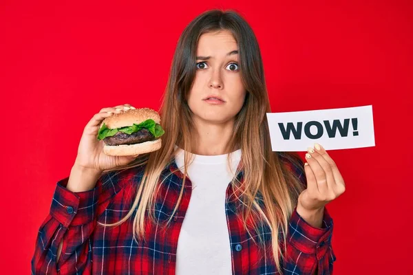 Beautiful Caucasian Woman Eating Tasty Classic Burger Holding Wow Text — Stock Photo, Image