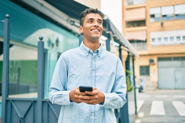 若いラテン語の男笑顔幸せな使用してスマートフォン街を歩く — ストック写真