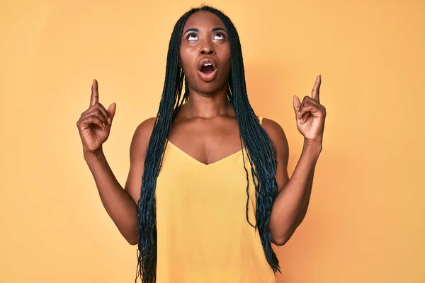 Африканская Американка Косичками Повседневной Одежде Удивлена Удивлена Глядя Вверх Указывая — стоковое фото