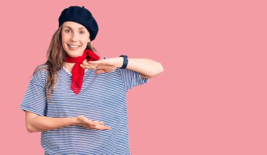 Fransız beresi ve çizgili tişört giyen genç ve güzel sarışın bir kadın. Ellerinde büyük ve büyük beden işareti olan bir jest. Ölçüm sembolü. Kameraya bakıp gülümsüyor. ölçüm kavramı. 