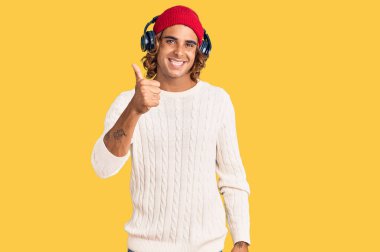 Kulaklıkla müzik dinleyen genç İspanyol adam elleriyle mutlu bir jest yapıyor. Kameraya bakıp başarıyı gösteren ifade. 