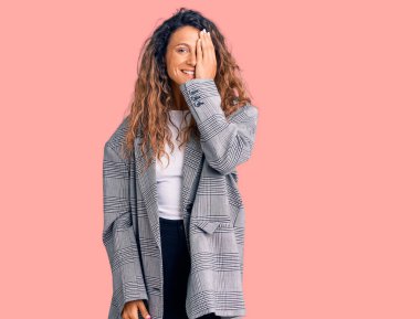 Dövmeli genç İspanyol kadın, iş elbisesi giyiyor. Bir gözünü eliyle kapatıyor. Yüzünde kendine güvenen bir gülümseme ve şaşırtıcı bir duygu var.. 