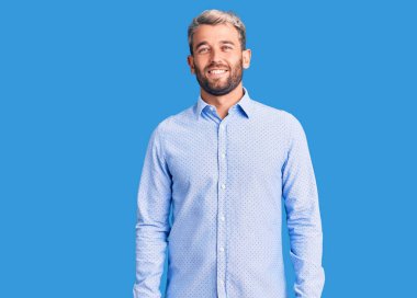 Yakışıklı sarışın, zarif gömlek giyen, yüzünde mutlu ve havalı bir gülümseme olan genç bir adam. şanslı kişi. 