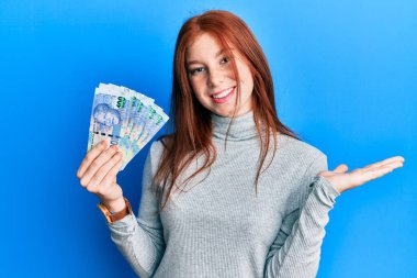 Genç kızıl saçlı kız Güney Afrika 'yı elinde tutuyor. 100 rand' lik banknotlar başarıyı mutlu bir gülümsemeyle ve kazanan ifadeyle kutluyor. 