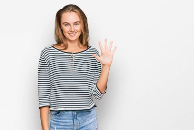 Güzel sarışın kadın gündelik kıyafetler giyer ve beş numarayı göstererek gülümserken kendinden emin ve mutluydu.. 