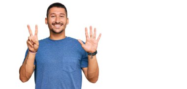 Dövmeleri olan yakışıklı bir adam. Günlük giysiler giyiyor. Yedi numarayı gösteriyor ve gülümsüyor.. 