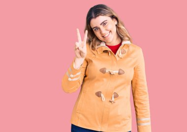 Gündelik giysiler giyen genç beyaz kadın iki numarayı gösterip işaret ederken kendine güvenen ve mutlu bir şekilde gülümsüyor.. 