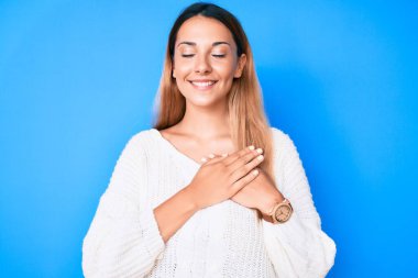 Genç esmer kadın, sıradan bir süveter giyiyor, elleri göğsünde, gözleri kapalı gülümsüyor ve yüzünde minnet ifadesi var. sağlık kavramı. 