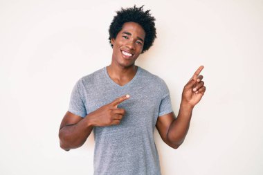 Yakışıklı Afro saçlı, sıradan giyinmiş, gülümseyen ve kameraya bakan iki eli ve parmakları yanda olan Afro-Amerikan bir adam.. 