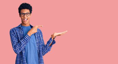 Genç Afro-Amerikan adam gündelik giysiler ve gözlük takıyor kameraya hayret ediyor ve gülümsüyor.. 