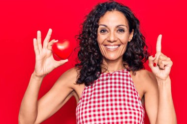 Orta yaşlı, kalbi olan güzel bir kadın bir fikirle ya da soruyla gülümsüyor ve mutlu bir yüzle işaret ediyor. 