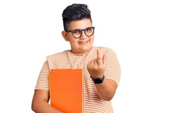 Küçük çocuk kitap tutuyor, gözlük takıyor, el kol hareketi yapıyor, mutlu karşılıyor ve gülümsüyor. 