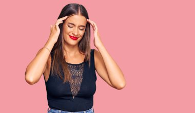 Elleri başının üstünde, günlük kıyafetler giyen genç İspanyol kadın, stres yüzünden baş ağrısı çekiyor. migren ağrısı. 