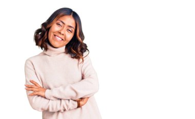 Balıkçı yaka kazak giyen, kollarını kavuşturup kameraya bakan güzel, melez bir kadın. pozitif kişi. 