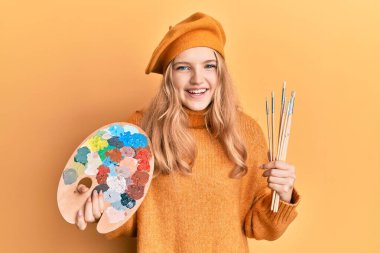 Güzel, beyaz bir kız elinde boya fırçası ve ressam paleti ile kahkahalarla gülüyor.. 