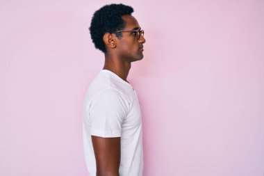 Sıradan kıyafetler ve gözlük takan Afrikalı yakışıklı bir adam yan tarafa bakıyor, rahat poz veriyor kendine güvenen bir gülümsemeyle doğal bir yüz ifadesi sergiliyor.. 