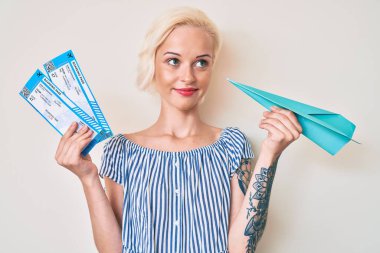 Elinde kağıt uçak ve uçuş kartı olan genç sarışın bir kadın. Gülümsüyor ve başka tarafa bakıyor.. 