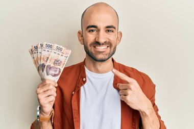 İspanyol asıllı genç adam 500 Meksika pesosu tutuyor. Gülümsüyor, mutlu bir şekilde parmakla işaret ediyor. 