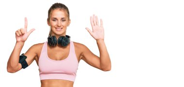 Spor kıyafetleri giyen ve kulaklık takan genç sarışın kadın yedi numaralı parmaklarını gösterip gösterirken kendinden emin ve mutlu bir şekilde gülümsüyor.. 
