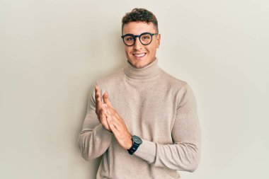 Balıkçı yaka kazak giyen İspanyol genç adam alkışlıyor ve alkışlıyor mutlu ve neşeli, gururlu elleri bir arada. 