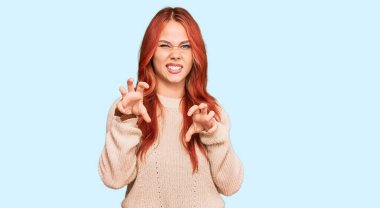 Kış süveteri giyen genç kızıl saçlı kadın komik bir şekilde gülümsüyor kedi gibi pençe hareketi yapıyor, agresif ve seksi bir ifade. 